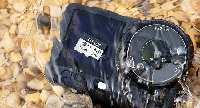 Action camera in a waterproof housing resting on wet pebbles with a Lexar memory card visible on the case La micro SDXC Silver Plus de LEXAR avec 2 To de stockage