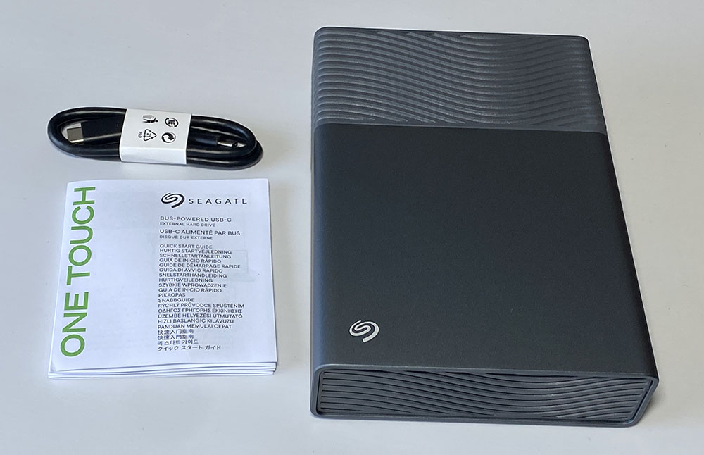 Test du disque dur externe 3,5" Seagate One Touch 8 To auto alimenté | Bhmag Seagate One Touch external hard drive with a USB-C cable and quick-start guide beside it on a light surface. Test du disque dur externe 3,5" Seagate One Touch 8 To auto alimenté