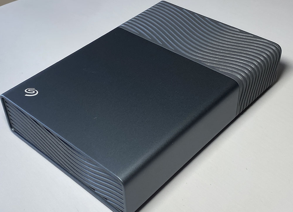 Test du disque dur externe 3,5" Seagate One Touch 8 To auto alimenté | Bhmag External portable hard drive with a dark gray body and a ridged wave pattern along the edges Test du disque dur externe 3,5" Seagate One Touch 8 To auto alimenté